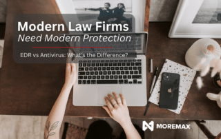 Top-down view of a home office workspace with a laptop, smartphone, notebooks, and framed photos on a wooden desk. Overlay text reads, "Modern Law Firms Need Modern Protection" and "EDR vs Antivirus: What's the Difference?" with the MoreMax logo displayed in the corner.
