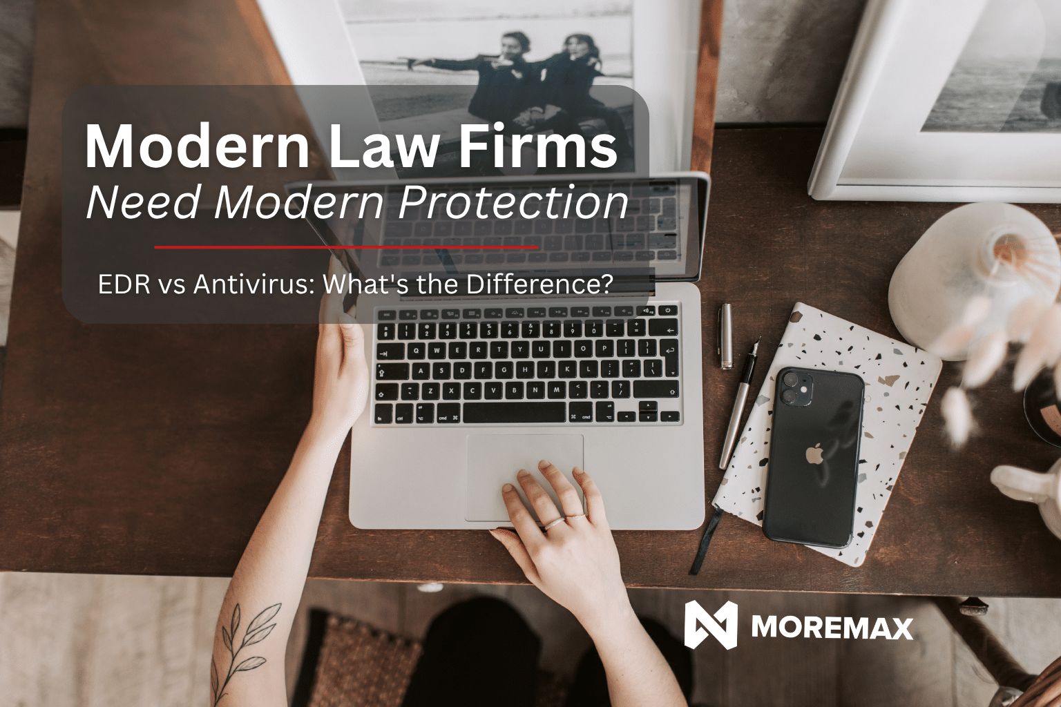Top-down view of a home office workspace with a laptop, smartphone, notebooks, and framed photos on a wooden desk. Overlay text reads, "Modern Law Firms Need Modern Protection" and "EDR vs Antivirus: What's the Difference?" with the MoreMax logo displayed in the corner.
